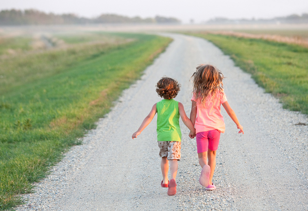 Children holding hands walking down a road.