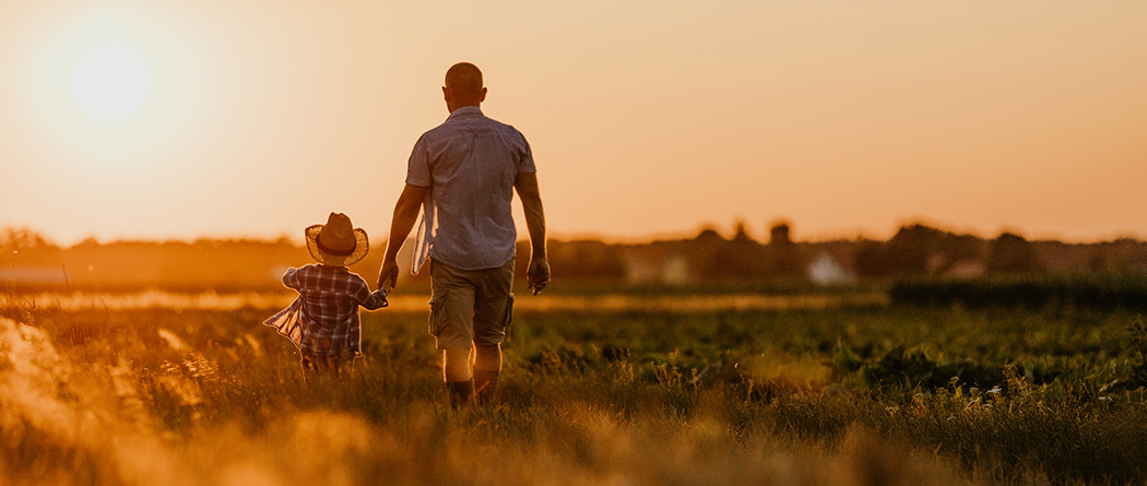 Farmer and child walking through a field at sunset.