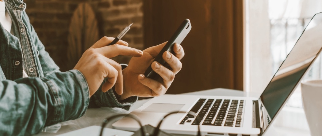 a person holding a mobile phone and working on their laptop