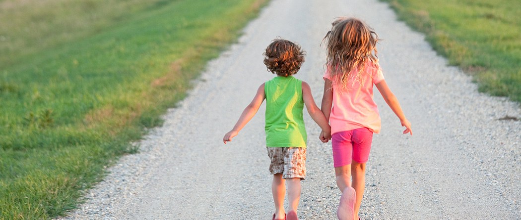 two kids holding hands walking down a dirt road